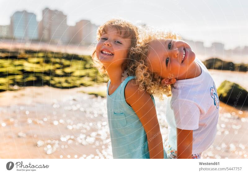 Porträt eines glücklichen kleinen Jungen und Mädchens, die Rücken an Rücken am Strand stehen Portrait Porträts Portraits Buben Knabe Knaben männlich weiblich