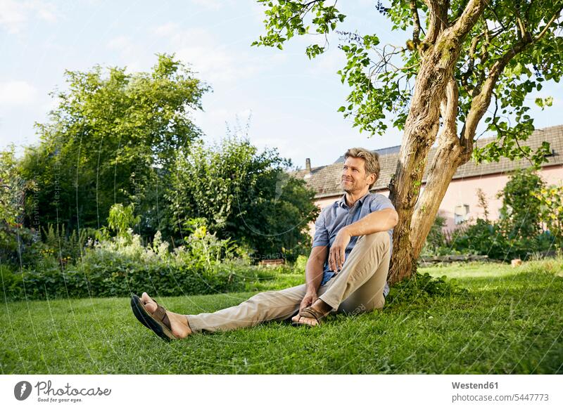 Reifer Mann steht in seinem Garten und trägt eine Schürze sitzen sitzend sitzt nachdenken überlegen Männer männlich anlehnen angelehnt lehnend Zuhause zu Hause