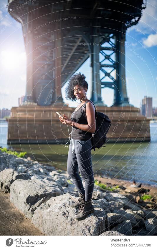 USA, New York City, Brooklyn, lächelnde Frau beim Musikhören unter der Manhattan Bridge Brücke Bruecken Brücken weiblich Frauen hoeren Erwachsener erwachsen