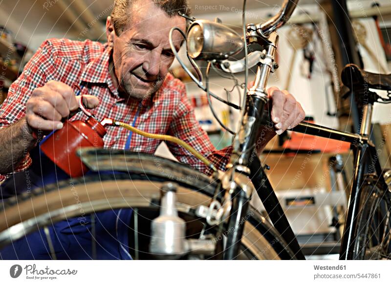 Älterer Mann ölt Fahrrad in seiner Werkstatt ein Bikes Fahrräder Räder Rad Senior ältere Männer älterer Mann Senioren Werkstätte Werkstaette Werkstaetten