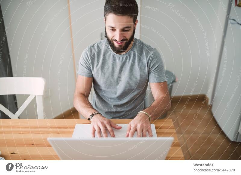 Junger Mann sitzt zu Hause und benutzt Laptop jung Männer männlich Websurfen Im Net surfen Surfen sitzen sitzend tippen Notebook Laptops Notebooks