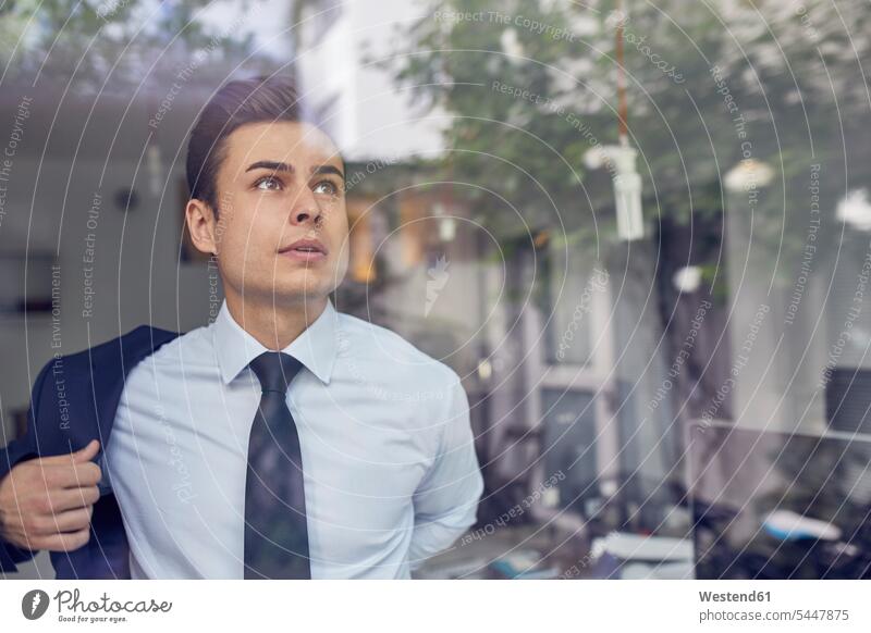Porträt eines jungen Geschäftsmannes hinter Glasscheibe im Büro, der seine Jacke anzieht Businessmann Businessmänner Geschäftsmänner Portrait Porträts Portraits
