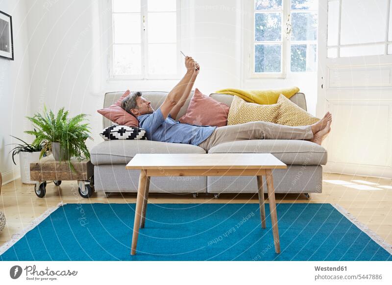 Mann liegt zu Hause auf dem Sofa und benutzt ein digitales Tablett Online Websurfen Im Net surfen Surfen bequem Zuhause daheim Männer männlich Entspannung