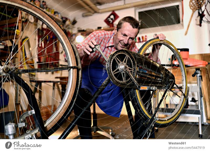 Älterer Mann überprüft Fahrrad in seiner Werkstatt Bikes Fahrräder Räder Rad Werkstätte Werkstaette Werkstaetten Werkstätten Senior ältere Männer älterer Mann