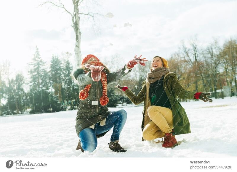 Zwei beste Freunde amüsieren sich im Schnee Freundinnen Freundschaft Kameradschaft lachen verschneit schneebedeckt hocken kauernd hockend Winter winterlich