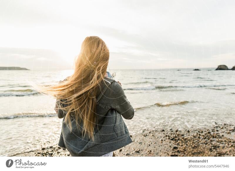 Junge Frau beobachtet den Sonnenuntergang am Strand Sonnenuntergänge weiblich Frauen Beach Straende Strände Beaches entspannt entspanntheit relaxt Stimmung