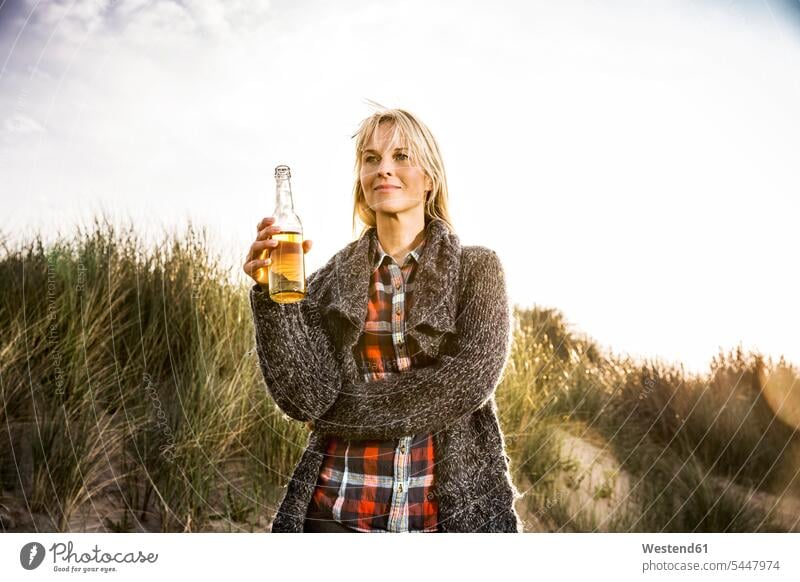 Lächelnde Frau trinkt ein Bier in den Dünen lächeln Strand Beach Straende Strände Beaches weiblich Frauen Sanddüne Sanddünen Erwachsener erwachsen Mensch