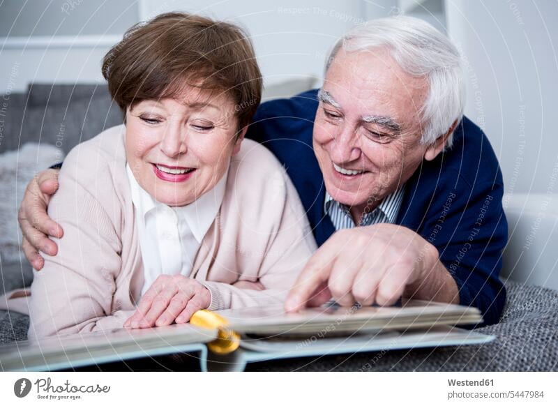 Älteres Ehepaar liegt auf dem Sofa und schaut sich ein Fotoalbum an Senioren alte ältere Fotos Fotoalben betrachten betrachtend liegen liegend Paar Pärchen