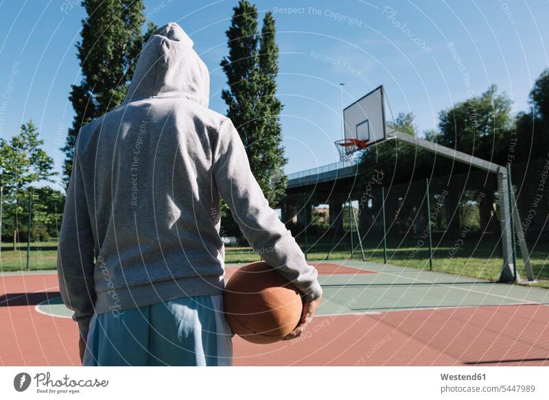 Mann hält Basketball, Korb im Hintergrund Basketbaelle Basketbälle Basketballspieler Basketballer halten Sport Männer männlich Freizeit Muße Erwachsener
