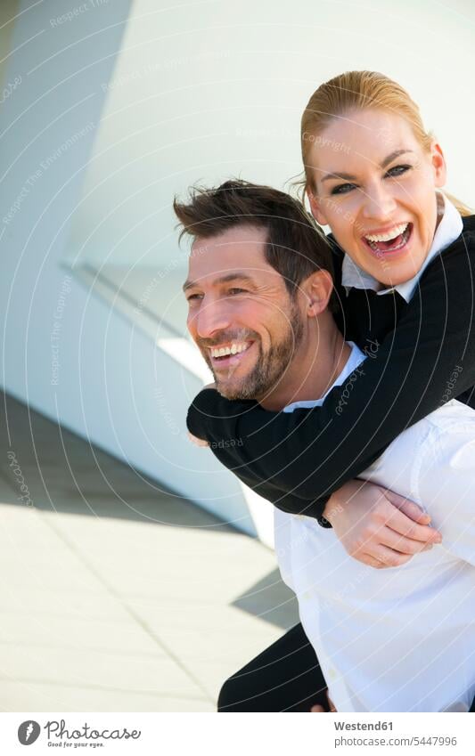 Porträt eines glücklichen Geschäftsmannes, der eine Frau huckepack trägt Glück glücklich sein glücklichsein Huckepack Spaß Spass Späße spassig Spässe spaßig