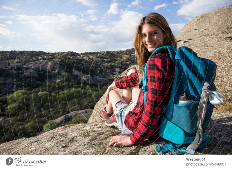 Spanien, Madrid, lächelnde junge Frau, die sich während eines Trekking-Tages auf einem Felsen ausruht weiblich Frauen wandern Wanderung Berg Berge sitzen
