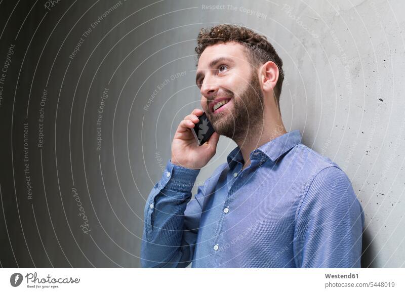 Lächelnder Mann am Handy an Betonwand lächeln telefonieren anrufen Anruf telephonieren Männer männlich Betonwände Betonwaende Mobiltelefon Handies Handys