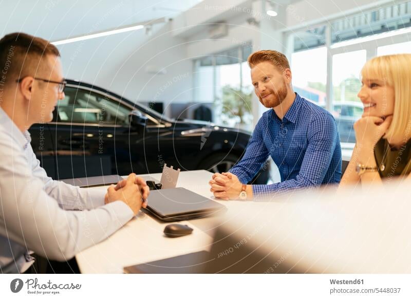 Verkäufer, der ein Paar im Autohaus berät Wagen PKWs Automobil Autos verkaufen Autohäuser Autohaeuser Autohandlung Autohandlungen Kauf besprechen diskutieren
