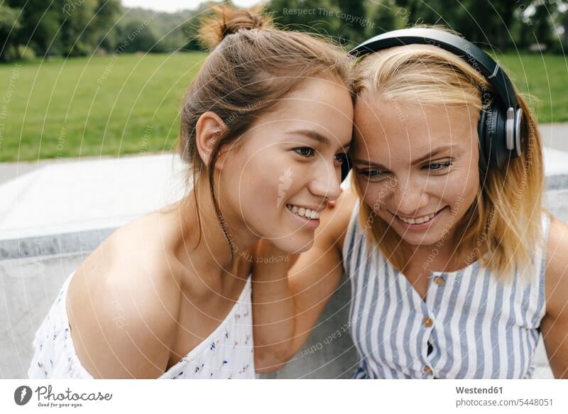 Zwei lächelnde junge Frauen teilen sich im Freien Kopfhörer Freundinnen Kopfhoerer weiblich glücklich Glück glücklich sein glücklichsein Teilen Sharing Freunde