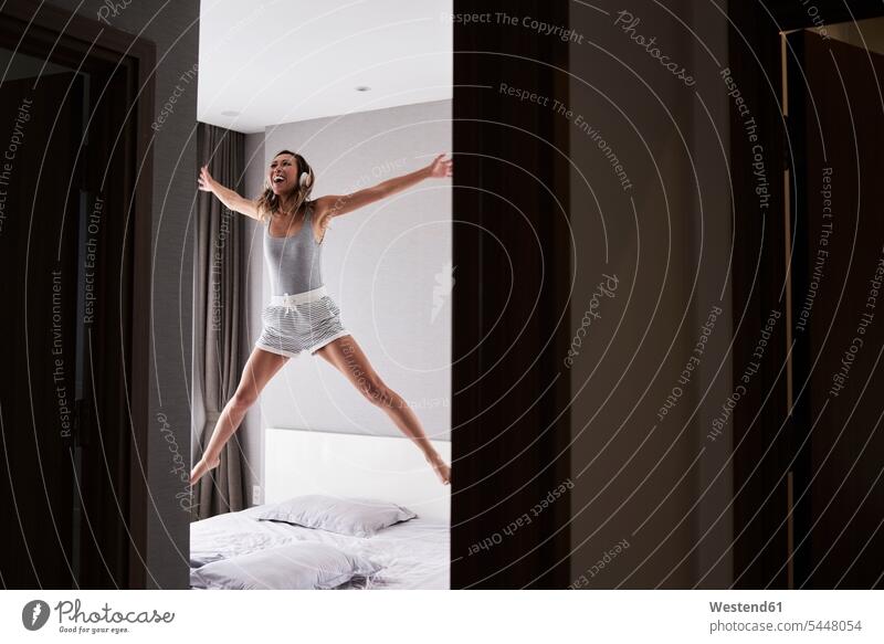 Aufgeregte Frau mit Kopfhörern springt im Bett springen hüpfen Kopfhoerer Betten weiblich Frauen Begeisterung Enthusiasmus Überschwang begeistert
