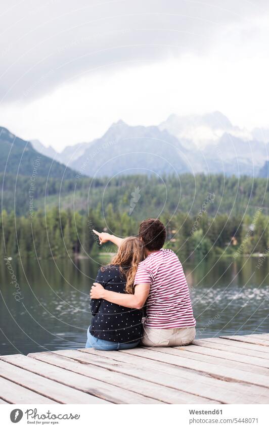 Rückenansicht eines jungen Paares, das auf einem Steg am See sitzt Seen Bootssteg Anleger Stege Landesteg Anlegestellen Landestege Bootsstege Pärchen