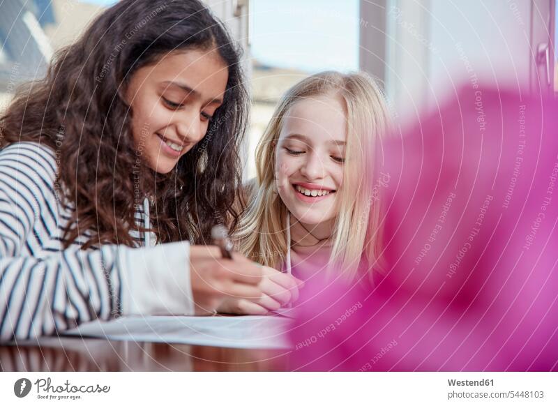 Zwei Mädchen machen gemeinsam Hausaufgaben lächeln weiblich schreiben aufschreiben notieren schreibend Schrift Freundinnen Kind Kinder Kids Mensch Menschen