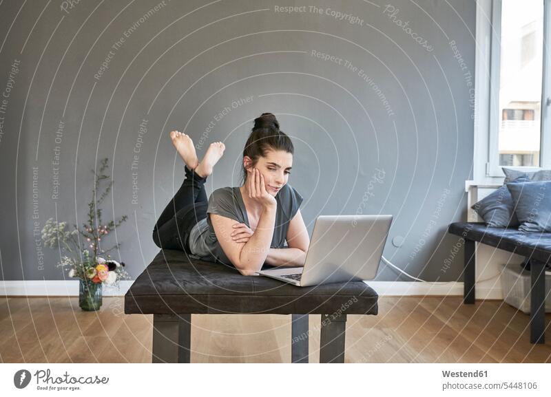Junge Frau liegt mit Laptop im Wohnzimmer liegen liegend Notebook Laptops Notebooks weiblich Frauen Computer Rechner Erwachsener erwachsen Mensch Menschen Leute