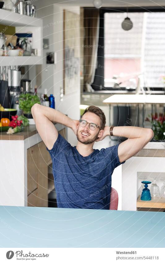 Porträt eines lächelnden jungen Mannes, der zu Hause am Küchentisch sitzt Zuhause daheim Tisch Tische Männer männlich sitzen sitzend Portrait Porträts Portraits