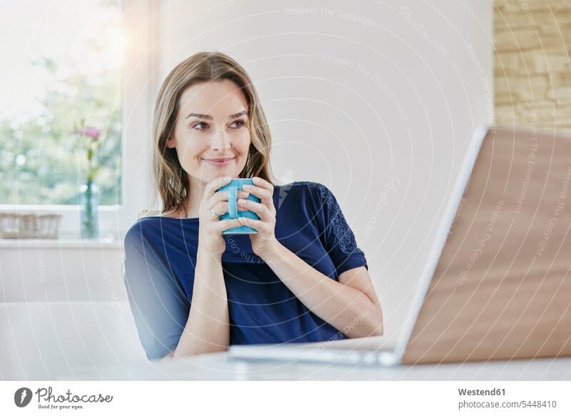 Lächelnde Frau zu Hause mit Kaffeetasse und Laptop Notebook Laptops Notebooks weiblich Frauen lächeln Computer Rechner Erwachsener erwachsen Mensch Menschen