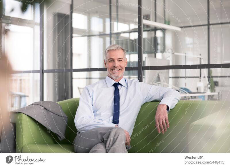 Ein reifer Geschäftsmann, der im Büro auf einer Couch sitzt Europäer Kaukasier Europäisch kaukasisch Sitzecke Dreiviertelansicht lächeln glücklich Glück