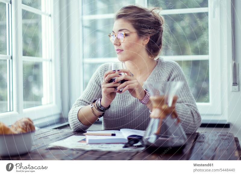 Junge Frau trinkt Kaffee am Tisch und schaut durchs Fenster weiblich Frauen Erwachsener erwachsen Mensch Menschen Leute People Personen trinken Brille Brillen