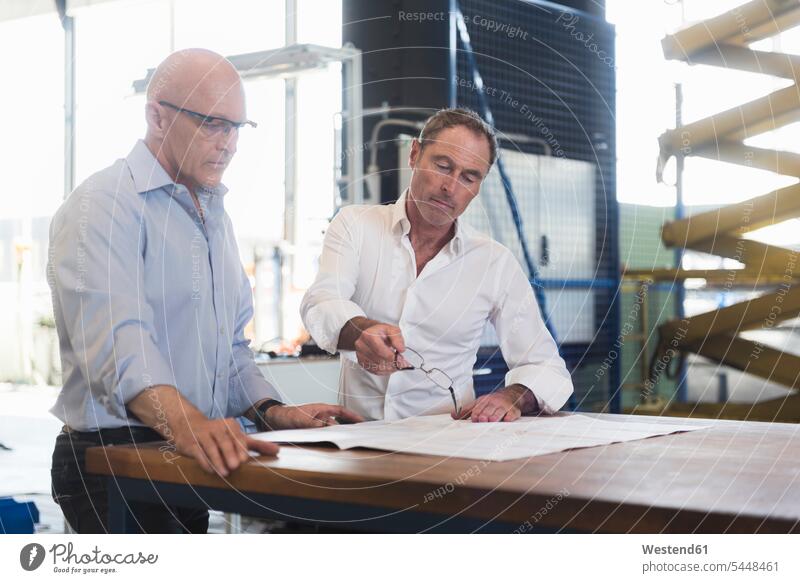Zwei Geschäftsleute sehen sich den Plan auf dem Tisch in der Fabrik an Fabriken Pläne Geschäftsmann Businessmann Businessmänner Geschäftsmänner sprechen reden