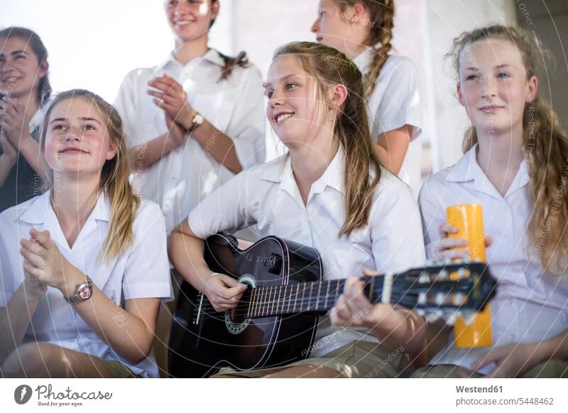 Weibliche Gymnasiastin spielt Gitarre mit einer Gruppe von Schulfreunden draußen Schülerin Bildung Saiteninstrument Musikinstrument Schule nur Teenagerinnen