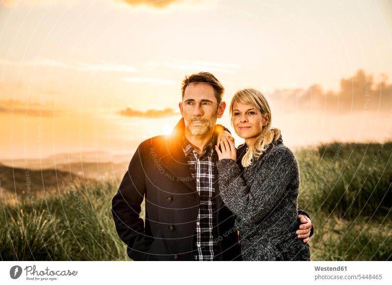 Ehepaar steht bei Sonnenuntergang in den Dünen Paar Pärchen Paare Partnerschaft Strand Beach Straende Strände Beaches Sanddüne Sanddünen lächeln Mensch Menschen