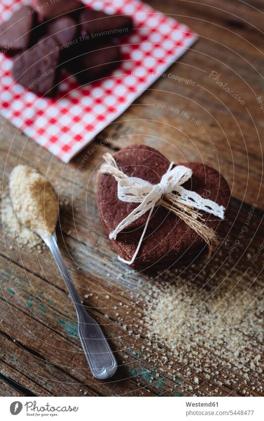 Stapel herzförmiger Schokoladen-Mürbekekse, gebunden mit Spitze und einem Teelöffel braunen Zuckers auf Holz Food and Drink Lebensmittel Essen und Trinken
