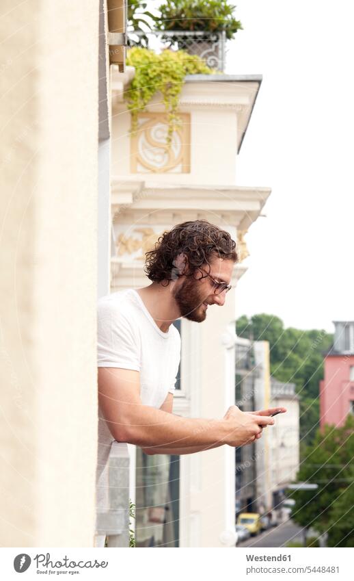 Lächelnder Mann auf dem Balkon mit Blick auf Handy Balkone Smartphone iPhone Smartphones Männer männlich Mobiltelefon Handies Handys Mobiltelefone Telefon