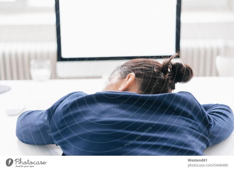 Rückenansicht einer überarbeiteten Frau, die im Büro auf dem Schreibtisch schläft Office Büros Geschäftsfrau Geschäftsfrauen Businesswomen Businessfrauen