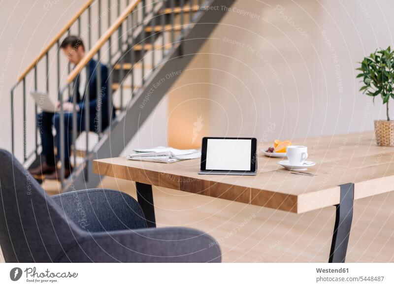 Tablett auf Tisch mit Geschäftsmann auf der Treppe mit Laptop im Hintergrund Businessmann Businessmänner Geschäftsmänner Notebook Laptops Notebooks Büro Office