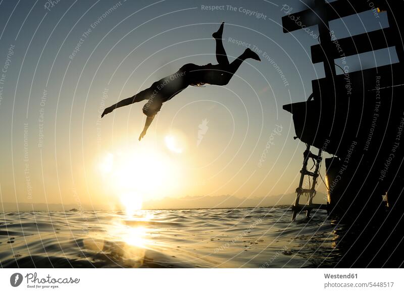 Mann springt bei Sonnenuntergang vom Steg ins Meer Meere Männer männlich springen hüpfen Urlaub Ferien Gewässer Wasser Erwachsener erwachsen Mensch Menschen