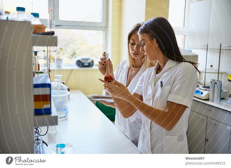 Zwei junge Frauen sehen sich im Labor Flüssigkeit in einem Kolben an ansehen weiblich Glaskolben Gemeinsam Zusammen Miteinander Flüssigkeiten flüssig Labore