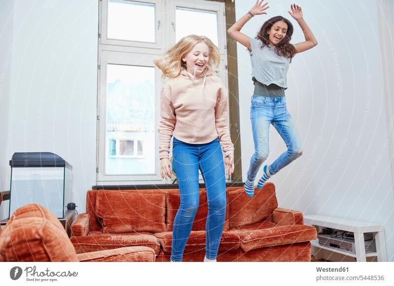 Zwei glückliche Mädchen springen und tanzen zu Hause weiblich hüpfen Freundinnen Spaß Spass Späße spassig Spässe spaßig lachen Kind Kinder Kids Mensch Menschen