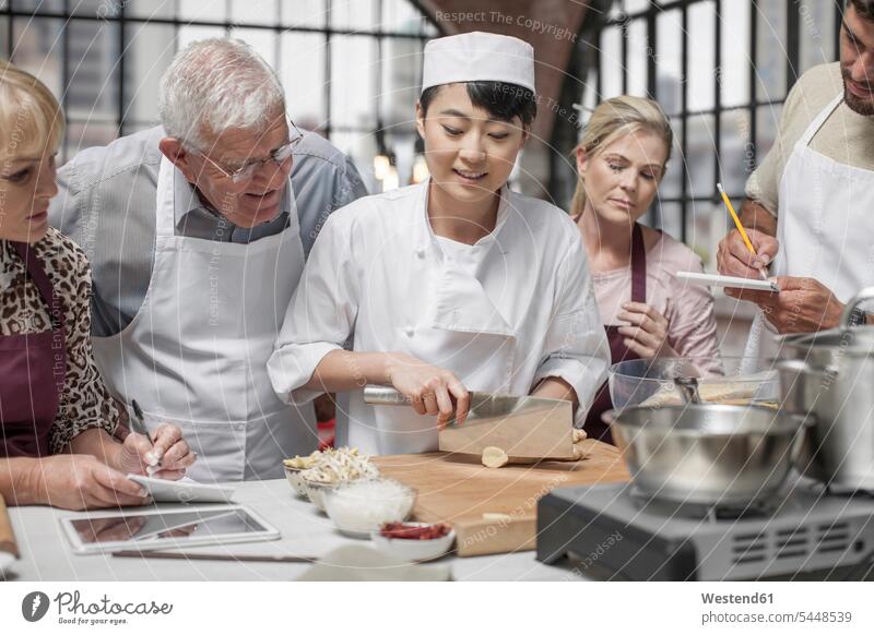 Teilnehmer eines Kochkurses sehen einer Köchin beim Zerkleinern der Zutaten zu Koechin Köchinnen Koechinnen kochen Gruppe Gruppe von Menschen Menschengruppe