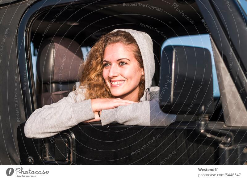 Porträt einer glücklichen jungen Frau, die sich aus dem Autofenster lehnt Portrait Porträts Portraits weiblich Frauen Wagen PKWs Automobil Autos Erwachsener