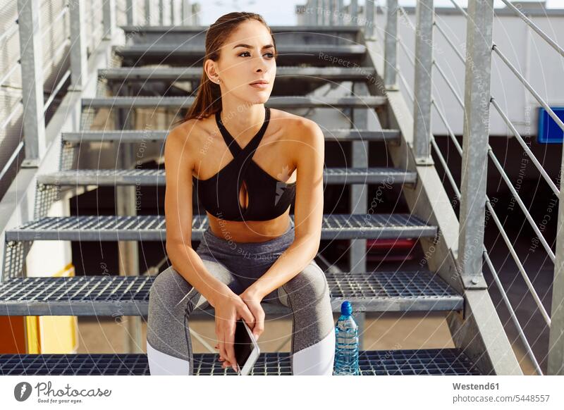 Frau macht Pause vom Training und hält Handy auf der Treppe sitzen sitzend sitzt trainieren Treppenaufgang weiblich Frauen Erwachsener erwachsen Mensch Menschen