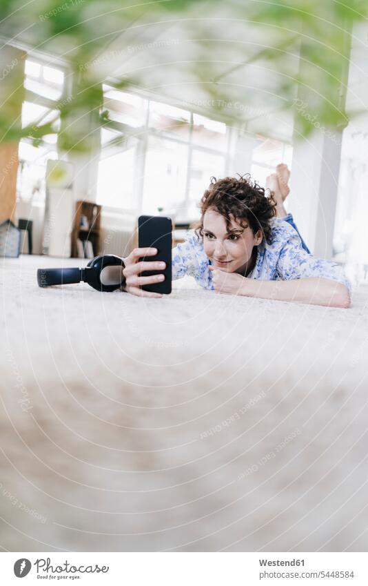 Frau liegt in ihrer Wohnung auf dem Boden und benutzt ein Smartphone wohnen Wohnungen Selfie Selfies liegen liegend weiblich Frauen Kopfhörer Kopfhoerer