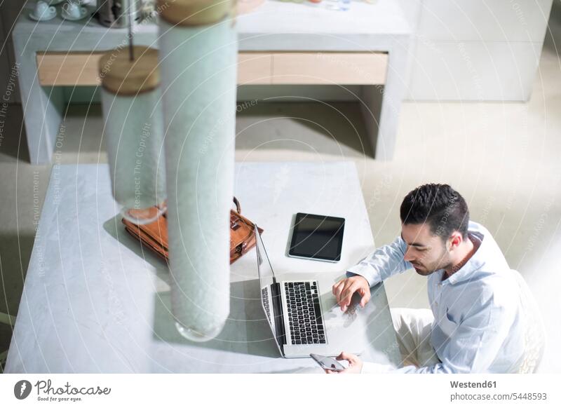 Junger Geschäftsmann, der im Büro arbeitet und mobile Geräte benutzt sitzen sitzend sitzt Mobilgeräte SMS Textnachricht arbeiten Arbeit Schreibtisch