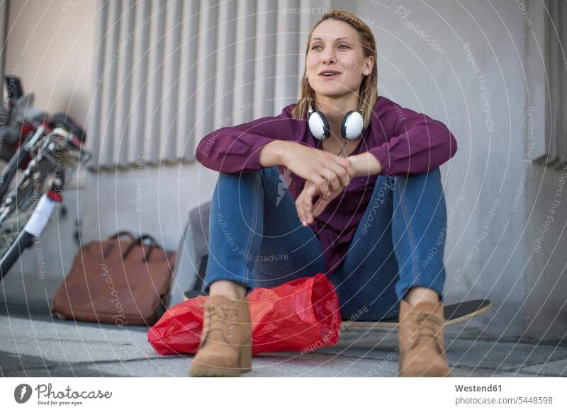 Junge Frau sitzt auf dem Skateboard auf der Straße Europäer Kaukasier Europäisch kaukasisch unkonventionell sitzen sitzend offenes Lächeln lachen