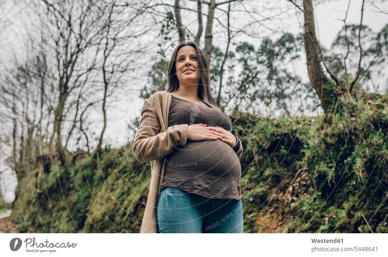 Lächelnde schwangere Frau im Wald im Herbst lächeln weiblich Frauen Schwangere Erwachsener erwachsen Mensch Menschen Leute People Personen stehen stehend steht
