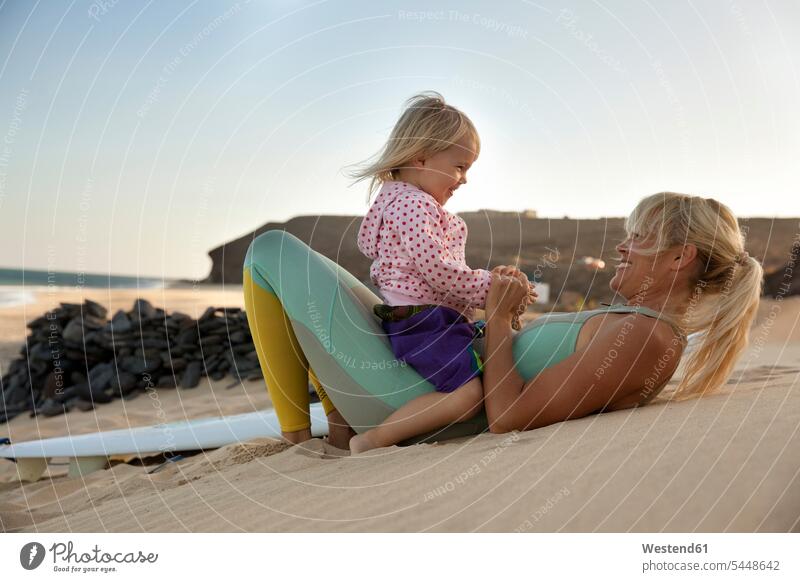 Spanien, Fuerteventura, glückliche Mutter und Tochter am Strand neben dem Surfbrett bei Sonnenuntergang Beach Straende Strände Beaches Töchter Mami Mutti Mütter