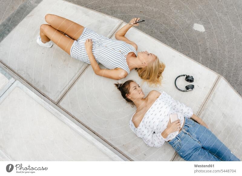 Zwei junge Frauen mit Handy und Kopfhörern in einem Skatepark Freundinnen Kopfhoerer Mobiltelefon Handies Handys Mobiltelefone Park Parkanlagen Parks