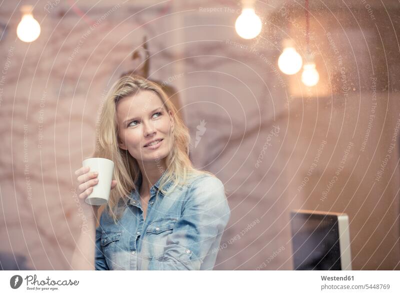 Porträt einer lächelnden blonden Frau mit Kaffeebecher, die aus dem Fenster schaut Portrait Porträts Portraits weiblich Frauen Erwachsener erwachsen Mensch