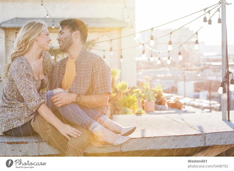 Glückliches Paar sitzt auf dem Dach und umarmt sich verliebt Dachterrasse Dachterrassen umarmen Umarmung Umarmungen Arm umlegen sitzen sitzend glücklich