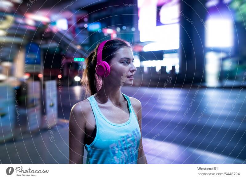 Junge Frau in rosa Sporthemd in moderner städtischer Umgebung bei Nacht trainieren junge Frau junge Frauen telefonieren anrufen Anruf telephonieren Kopfhörer