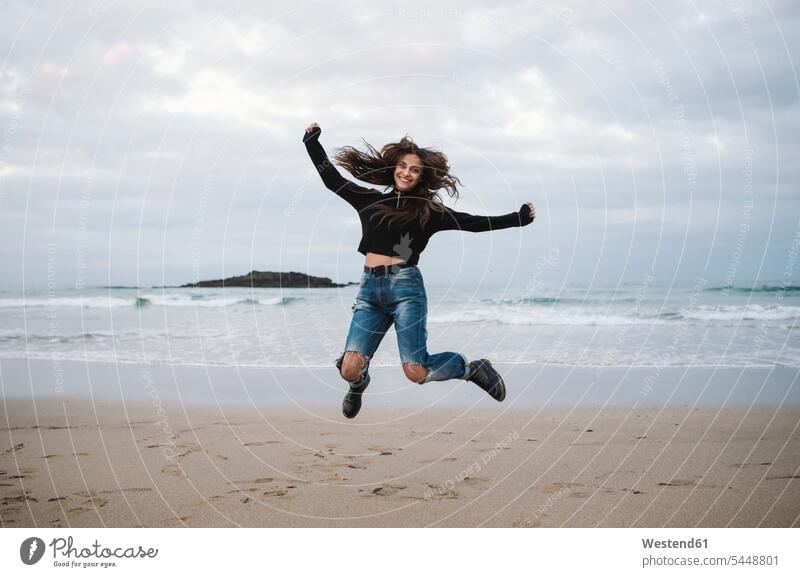 Glückliche Frau springt am Strand in die Luft Beach Straende Strände Beaches Freudensprung Luftsprung weiblich Frauen freuen Erwachsener erwachsen Mensch