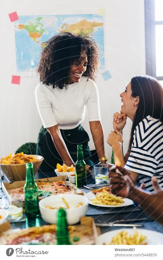 Zwei glückliche junge Frauen am Esstisch Pizza Pizzen Freunde lachen Tisch Tische essen essend Bier Essen Food Food and Drink Lebensmittel Essen und Trinken